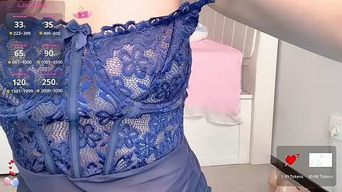 Media: Video of a woman wearing a blue lace bra with intricate floral patterns, standing in a white bathroom with a pink towel hanging on a hook.