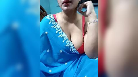 Media: Video of a South Asian woman in a blue sari with white floral embroidery, wearing a red bra, talking on a phone.