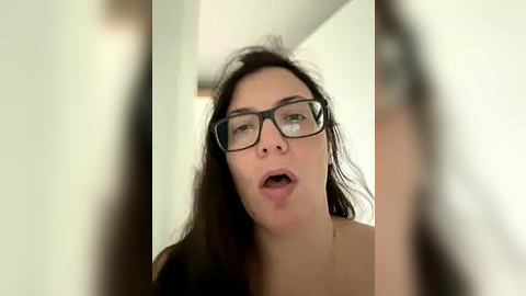 Media: A video of a young woman with long brown hair and glasses, mouth slightly open, appearing startled or shocked. Background is blurred, possibly a bathroom.