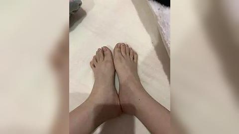 Media: Video of a pair of pale, slender feet with neatly trimmed toenails, lying on a white marble surface, partially obscured by out-of-focus foreground.