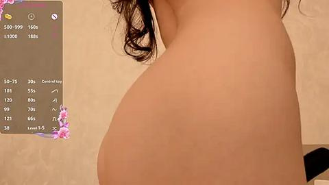 Media: Video of a nude woman's curvaceous backside, with a digital overlay displaying social media metrics. The background is a beige wall, and the woman has long, wavy brown hair.