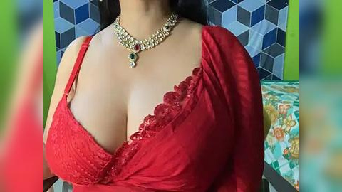 Media: Video of a woman with medium skin tone, wearing a red lace bra and a matching saree, adorned with a gold necklace featuring a large green stone. Background features geometric tiles and a colorful bedspread.