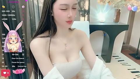 Media: Video of an Asian woman with long, straight hair, wearing a white strapless top and a fluffy robe, sitting indoors. A virtual bunny filter overlays her face.