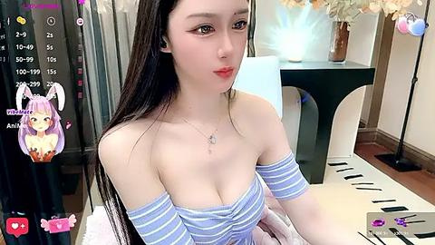 Media: Video of an Asian woman with long black hair and light skin, wearing a blue striped off-shoulder top, sitting at a desk with a smartphone, and a virtual character overlaid on the image.