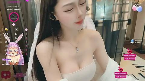 Media: Video of an Asian woman with long dark hair and a fair complexion, wearing a strapless white top, sitting in a dimly lit room.