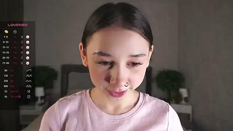 Media: A young Asian woman with straight black hair, wearing a light pink shirt, stands indoors, focusing intently on her phone. A digital menu with emojis and options is overlaid on the image.