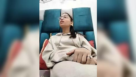 Media: A video of an Asian woman in a beige hoodie, wearing glasses, sitting in a reclined airplane seat with teal and red pillows, looking tired and relaxed.