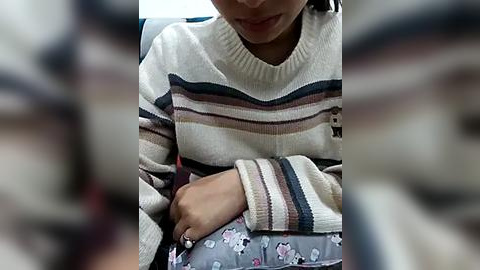 Media: Video of a young child with light skin, wearing a striped sweater and floral-patterned pants, seated on a car seat, with blurred background.