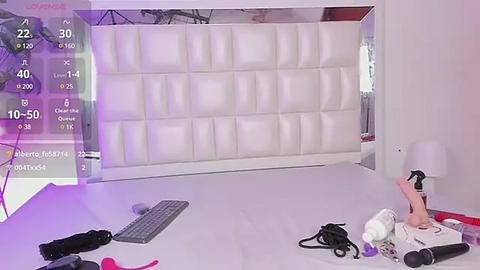 Media: Video of a modern, minimalist bedroom with a white tufted headboard, white walls, and a white floor. A white lamp and a gray keyboard lie on the floor.