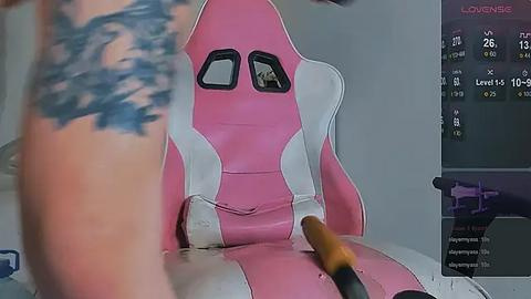 Media: Video of a person with a tattooed arm, seated in a pink and white gaming chair, holding a controller, set against a background of a computer monitor displaying a \"LOVEBEAT\" game interface.