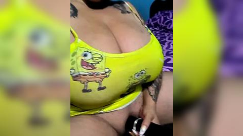 Media: A video of a busty woman in a bright yellow bikini top featuring SpongeBob SquarePants. She has a tattoo on her right arm. Her left hand is partially visible holding a black object.