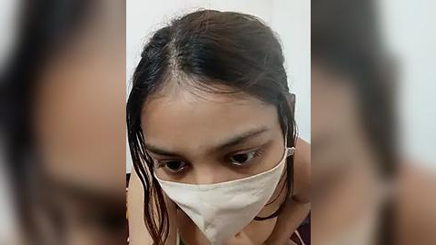 Media: A close-up video of a young Asian woman with long, wet, dark hair, wearing a white face mask, focused intently on her task.