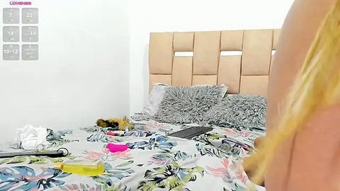 Media: A video of a messy bedroom with a woman lying on a bed, surrounded by scattered clothes, shoes, and a laptop. The headboard is upholstered in beige tufted fabric.