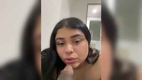 Media: A video of a young woman with medium brown skin, long black hair, and full lips, making a pouty face. The background shows a blurred bathroom with a white sink and beige walls.