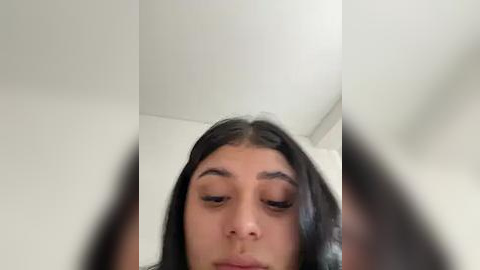 Media: Video of a young woman with long, straight black hair, light brown skin, and closed eyes. She is indoors with a white ceiling and soft, natural lighting.