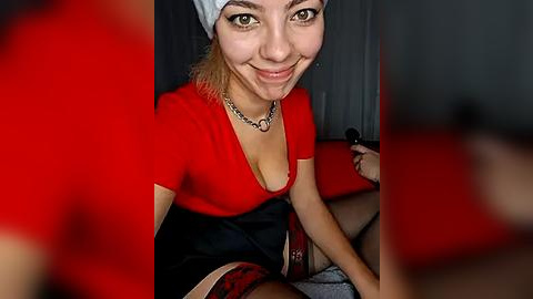 Media: A video of a young, smiling woman with light skin, wearing a red top, black shorts, and a white headband. She sits on a red couch with a gray background.