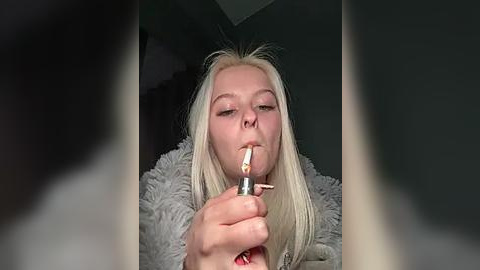 Media: Video of a blonde woman smoking a cigarette, wearing a gray, fuzzy sweater. She appears to be in a dimly lit room with blurry, dark backgrounds.