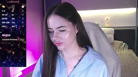 Media: A video of a young woman with long brown hair, wearing a light blue shirt, sitting in a modern bedroom with a bed and a colorful starry-night-themed screen in the background.