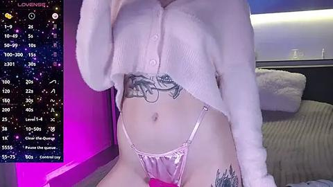 Media: A video of a light-skinned woman with tattoos, wearing a white cropped sweater and pink thong, standing in a bedroom with a bed and a window.