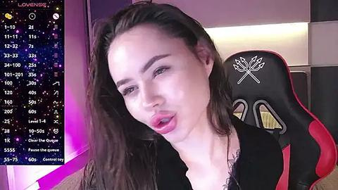 Media: Video of a young woman with long brown hair, wearing a black top, sitting in a gaming chair, lips slightly parted, with a digital overlay of streaming stats in the background.