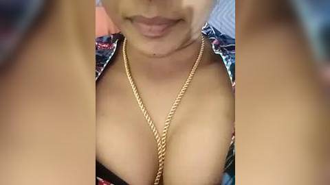 Media: Video of a light-skinned woman with medium-sized breasts, wearing a floral-patterned blouse unbuttoned to reveal cleavage, and a gold chain necklace. The background is blurred, focusing attention on her chest and face.