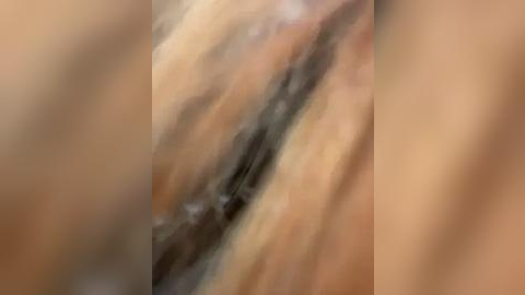 Media: This image is a blurred video depicting a close-up view of skin with visible pores and slight color variation, likely of human origin. The texture appears smooth with a slightly oily sheen. The background is indistinct, emphasizing the focus on the skin detail.