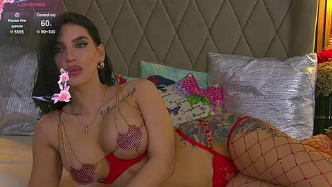 Media: A video of a Latina woman with dark hair and tattoos, lying on a bed in red lingerie and fishnet stockings, surrounded by colorful pillows.