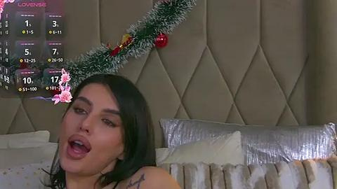 Media: A video of a dark-haired woman with a tattoo on her shoulder, wearing a Christmas headband, lying on a bed with festive decorations.