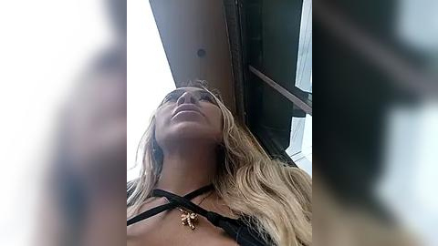 Media: Video of a blonde woman with fair skin, wearing a black strappy top, standing in an airplane window, looking upward, with blurred figures in the foreground.