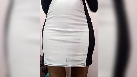 Media: Video of a slim, light-skinned woman wearing a tight, short, black-and-white dress with a zipper in the center, against a blurred background.