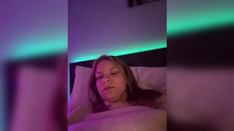 Media: A video of a Caucasian woman with light brown hair, sleeping peacefully under soft white bedding, with ambient purple lighting creating a serene, cozy atmosphere.