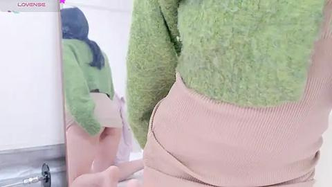 Media: Video of a person wearing a green and beige fuzzy costume, with their backside and reflection in a mirror visible.