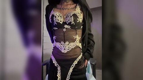 Media: Video of a person wearing a black corset with intricate gold lace detailing, a black jacket, and blue jeans. The background is dimly lit, creating a moody atmosphere.