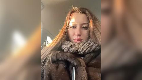 Media: Video of a blonde woman with messy hair, wearing a fur coat and scarf, sitting in a car, blurred background, sad expression.