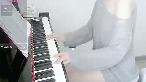 Media: A video of a woman with fair skin and light brown hair playing a digital piano, wearing a loose gray sweater, in a white room.