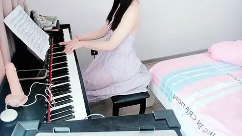 Media: Video of a young woman with long black hair, wearing a light purple dress, playing a digital keyboard in a bedroom. A pink and blue striped bedsheet is visible in the background.