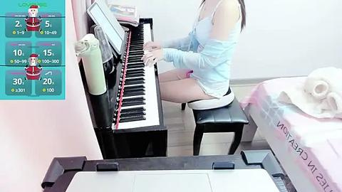 Media: A video of an Asian woman in a light blue top playing a keyboard in a brightly lit room. The background shows a bed with a pink blanket.