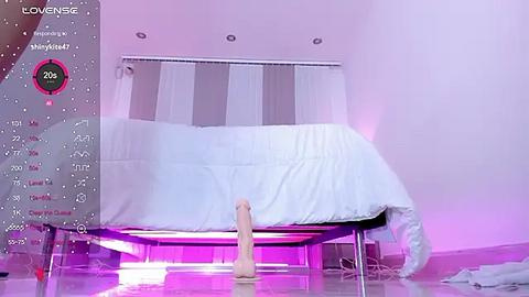 Media: A video of a modern, minimalist bedroom with a white bed, pink lighting, and a large, realistic sex toy. The room is clean and uncluttered.