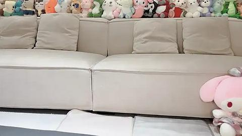 Media: Video of a beige sectional sofa with plush cushions, surrounded by a variety of plush toys, including Hello Kitty and My Melody, in a bright, cozy room with a white floor.