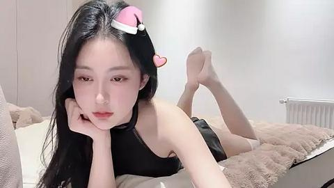 Media: A video of an Asian woman with long black hair, wearing a black choker and a Santa hat, lying on a beige bed, in a minimalist bedroom.