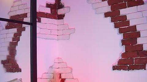 Media: Video of a partially demolished brick wall, with white and red bricks exposed, set against a pale purple backdrop, creating a surreal, abstract art piece.
