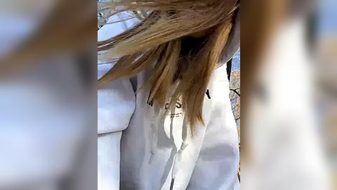 Media: Video of a person with long, light brown hair partially covering their face, wearing a white coat, standing in a snowy outdoor environment.