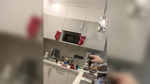 Media: A blurry video of a modern kitchen with white cabinets, a red apron, and a hand holding a camera.