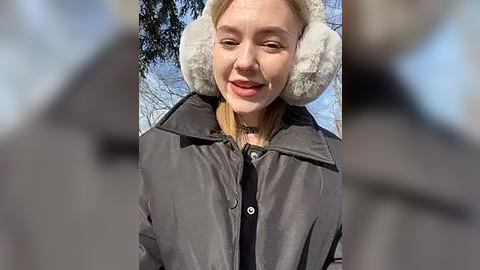 Media: Video of a smiling blonde woman in a fur-lined parka against a snowy backdrop. Her skin is fair, and she wears a choker necklace.