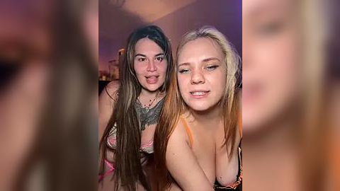 Media: Video of two young women, one with long brown hair, wearing a lace bra, and the other with blonde hair, smiling, in a dimly lit room.