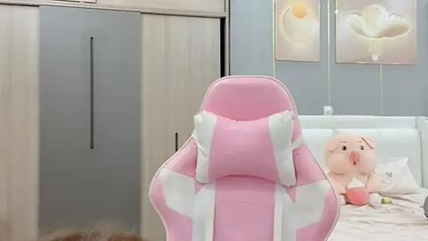 Media: Video of a pink and white gaming chair in a minimalist bedroom with a plush white bear, floral wallpaper, and light blue walls.