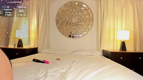 Media: A video of a well-lit bedroom with a large circular mandala wall art, white curtains, a white bed, and two dark wooden nightstands with lamps.