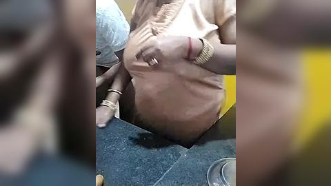 Media: Video of a woman with a medium to light skin tone, wearing a beige shirt, lying on a blue carpeted floor. Her left hand is touching her chest. A yellow object is nearby.