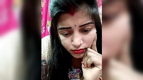 Media: Video of a young South Asian woman with long black hair, wearing a colorful sari with intricate patterns, and a bindi on her forehead, looking pensive with her hand to her chin.