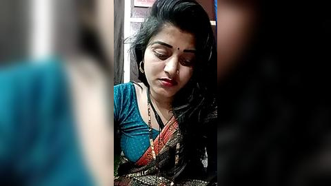 Media: Video of a young Indian woman in a blue and black sari, with a contemplative expression, in an urban setting.